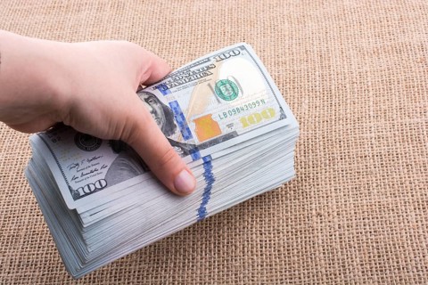 Hand holding banknote bundle of US dollar on a linen canvas background