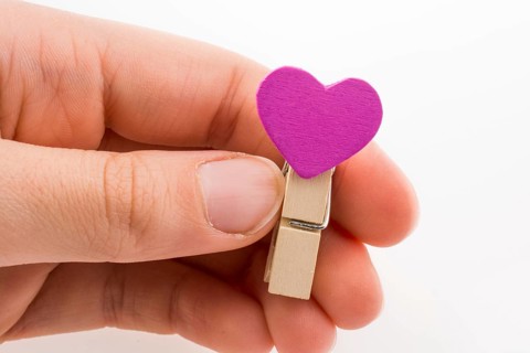 Hand holding a red clothespin with a heartshape on a white background