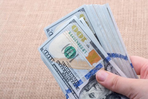 Hand holding banknote bundle of US dollar on a linen canvas background