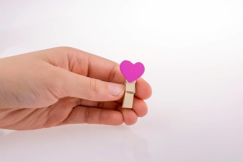 Hand holding a red clothespin with a heartshape on a white background
