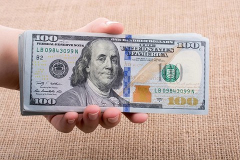 Hand holding banknote bundle of US dollar on a linen canvas background