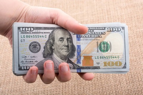 Hand holding banknote bundle of US dollar on a linen canvas background