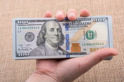 Hand holding banknote bundle of US dollar on a linen canvas background