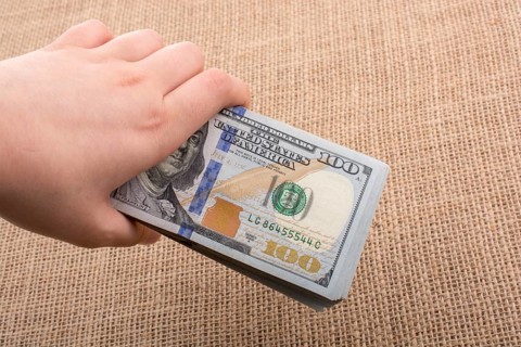 Hand holding banknote bundle of US dollar on a linen canvas background