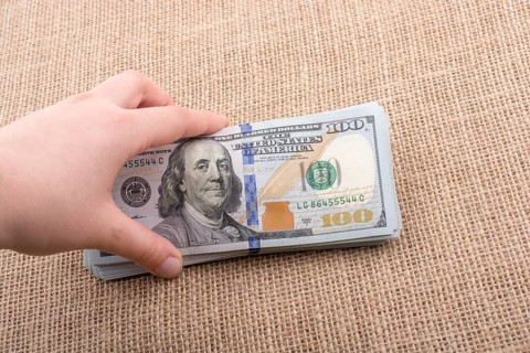 Hand holding banknote bundle of US dollar on a linen canvas background