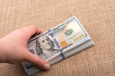Hand holding banknote bundle of US dollar on a linen canvas background