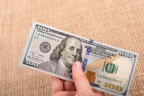 Hand holding banknote bundle of US dollar on a linen canvas background