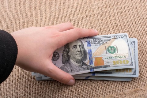 Hand holding banknote bundle of US dollar on a linen canvas background