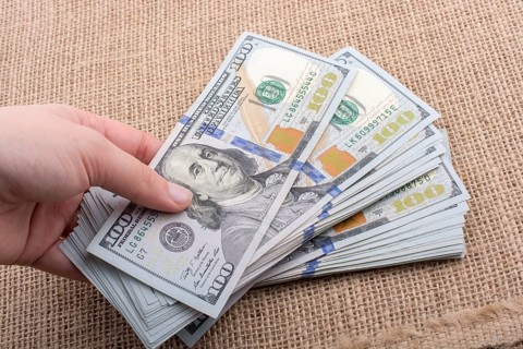 Hand holding banknote bundle of US dollar on a linen canvas background