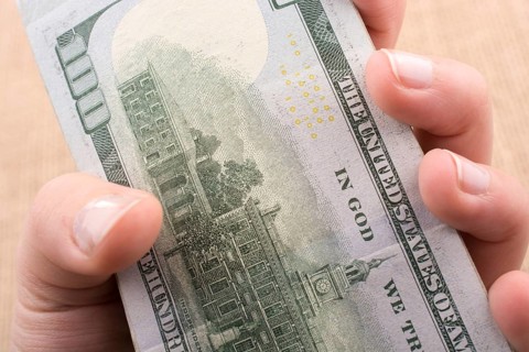 Hand holding banknote bundle of US dollar on a linen canvas background