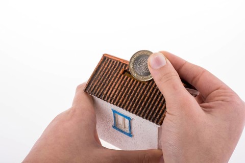 Hand dropping coin into the moneybox in the shape of a model house