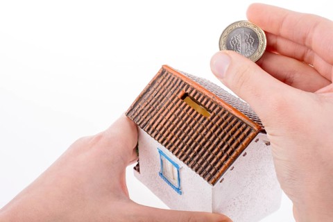 Hand dropping coin into the moneybox in the shape of a model house