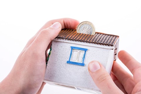 Hand dropping coin into the moneybox in the shape of a model house