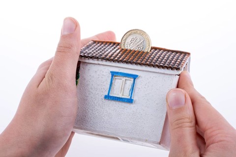 Hand dropping coin into the moneybox in the shape of a model house