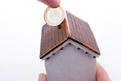 Hand dropping coin into the moneybox in the shape of a model house