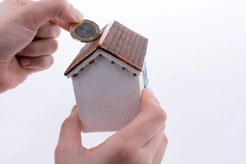 Hand dropping coin into the moneybox in the shape of a model house