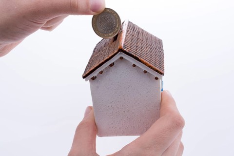 Hand dropping coin into the moneybox in the shape of a model house