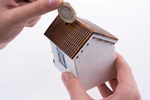 Hand dropping coin into the moneybox in the shape of a model house