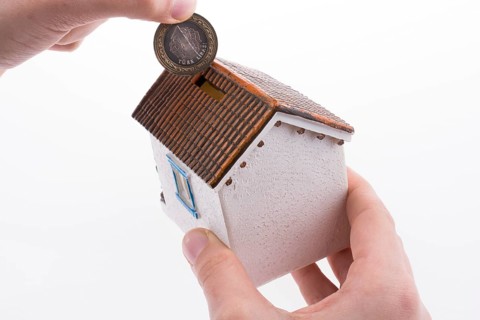 Hand dropping coin into the moneybox in the shape of a model house