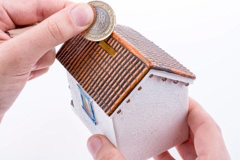 Hand dropping coin into the moneybox in the shape of a model house
