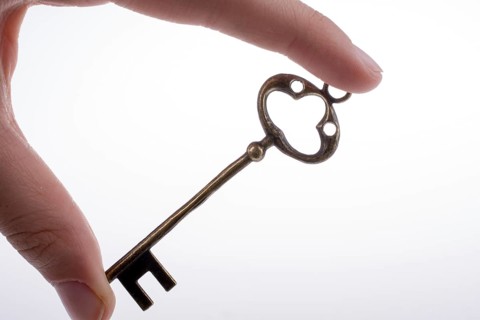 Hand holding a retro styled metal key on a white background