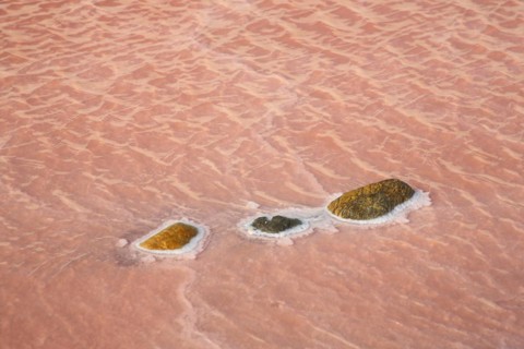 Red salt water with three stones with salt deposit at saline