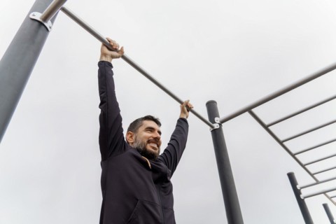 Young man dressed in black training on a pull-up bar in an outdoor gym