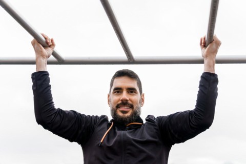 Young man dressed in black training on a pull-up bar in an outdoor gym