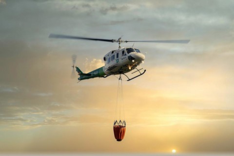 Firefighting helicopter in mid-flight dropping water with the sky red from the flames of the fire
