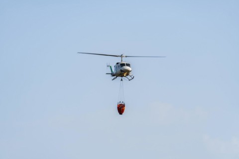 Firefighting helicopter in mid-flight dropping water bag on flames