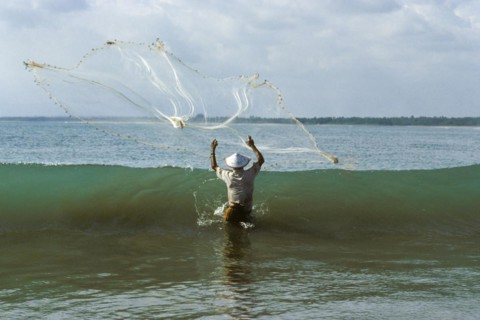 Fisherman with cast net in front of wave