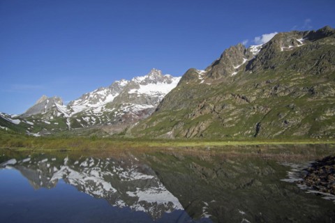 Reflection of mountains of the Mont Blanc massif and the Limestone Pyramids in water of Lago Combal lake in Val Veny in the Italian Alps