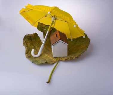Little model house placed on an Autumn leaf and under an umbrella