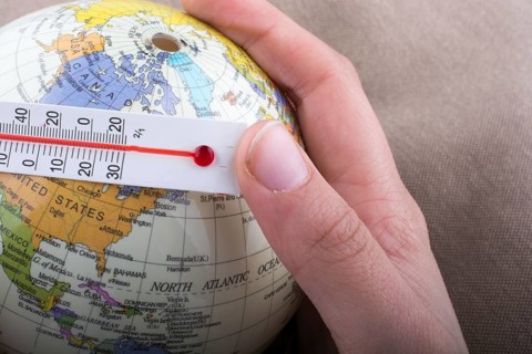Hand placing a thermometer on a little model globe