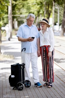 Elderly couple waiting for the tram at a stop with a smartphone in hand