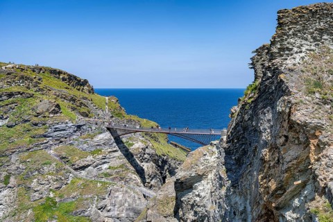 Tourists walk across the new footbridge to the peninsula with the castle ruins of Tintagel Castle