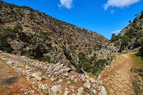 Dynamic composition of typical Greek or Cretan landscape with hills or mountains full of fresh spring greenery and paved paths crossing. Clear blue sky and clouds in spring daytime. Avlaki gorge of Ak...