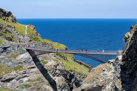 Tourists walk across the new footbridge to the peninsula with the castle ruins of Tintagel Castle