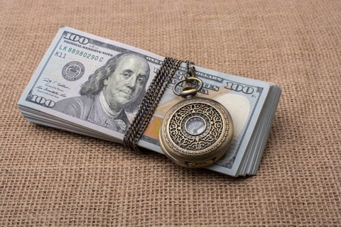 Pocket watch wrapped around banknote bundle of US dollar