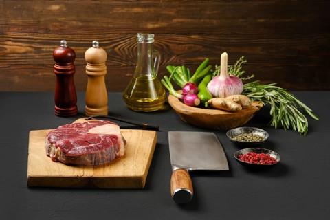 Raw beef shank cross-cut on chopping board with ingredients for cooking