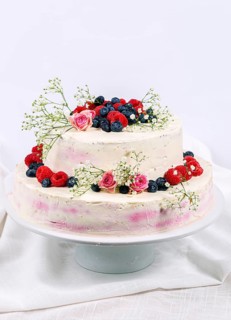Summery fresh two tier wedding cake decorated with berries and flowers festive cream cake on light background