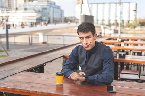 Business man sitting in a bar pointing at his watch looks disgusted at the camera. Delay concept
