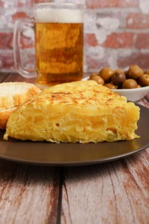 Typical spanish potato omelette freshly made on a wooden table with a fresh pitcher of beer