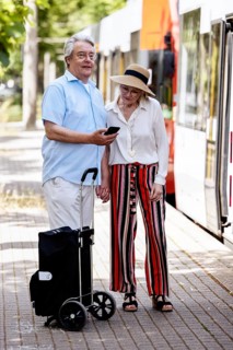 Elderly couple waiting for the tram at a stop with a smartphone in hand