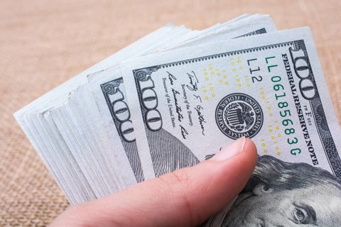 Hand holding banknote bundle of US dollar on a linen canvas background