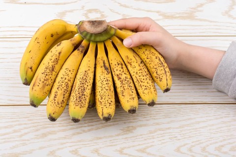 Hand holding bunch of freckled bananas on a wooden texture