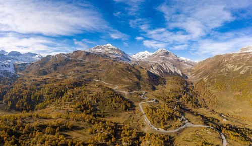 Aerial view over Val Poschiavo with its larch forests in autumn dress and the Bernina Pass road
