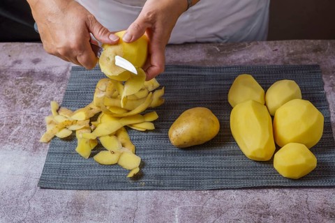Close-up of a woman's hands in a white apron peeling potatoes with a knife