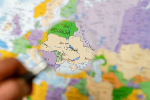 Hand of a man holding a magnifying glass looking at ukraine on a map of the world