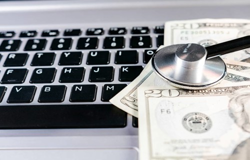 Stethoscope on dollar bills on top of laptop keyboard. Stethoscope on top of money on laptop keyboard